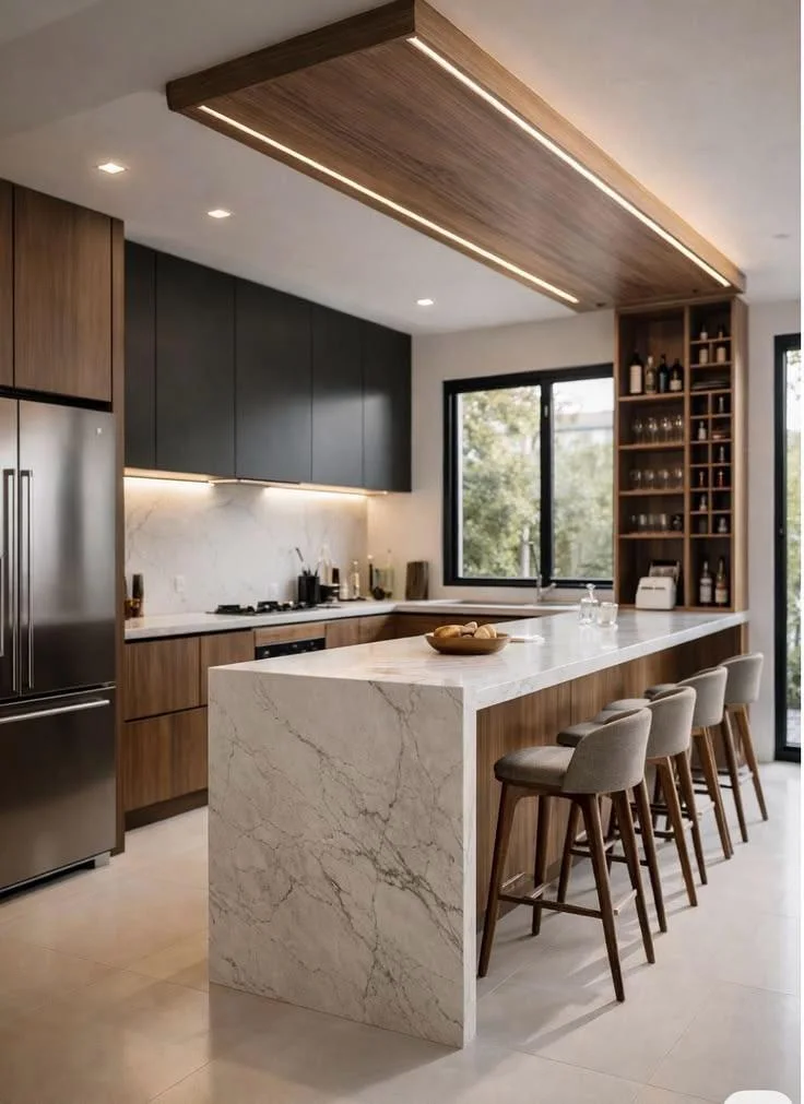 Open-plan kitchen with a waterfall marble island, bar stools, walnut and charcoal cabinetry and a lit wood ceiling feature